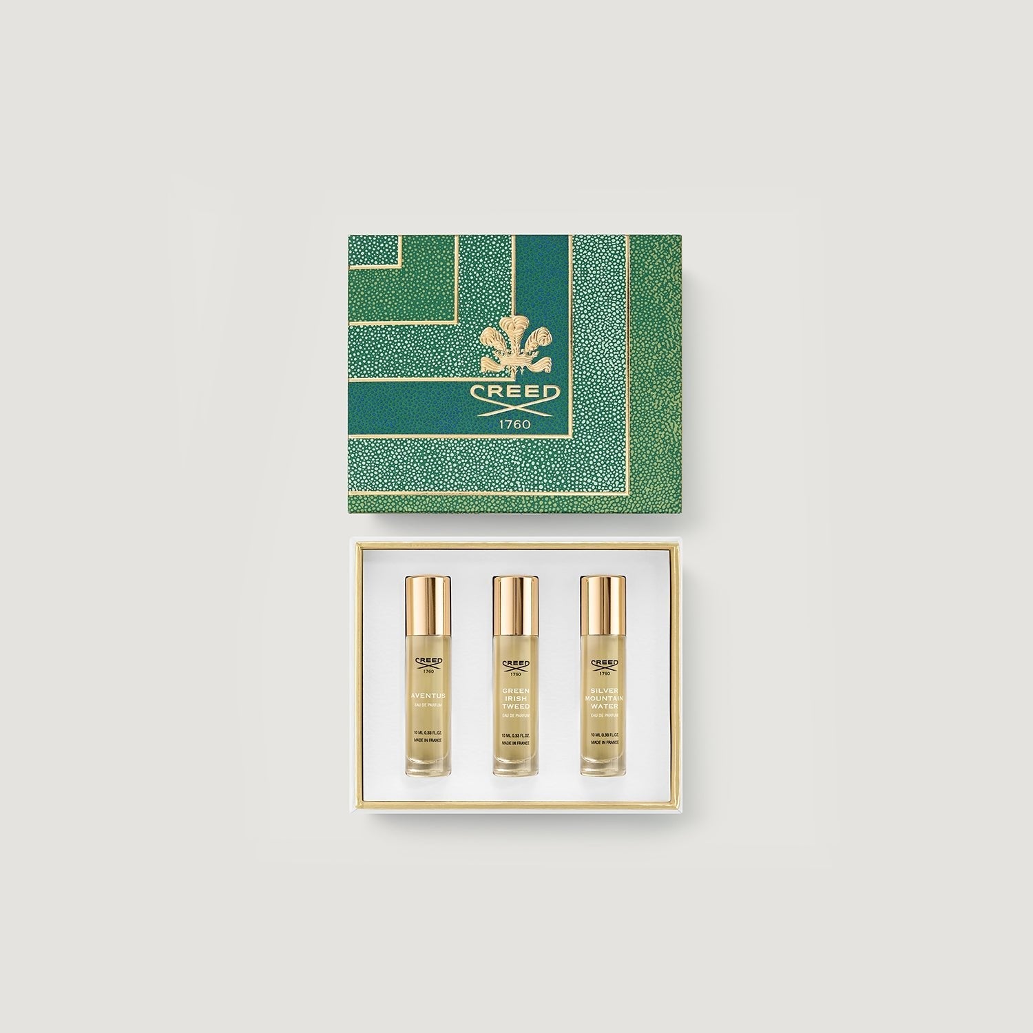 Three Creed perfume bottles in a gold and green box on a grey background