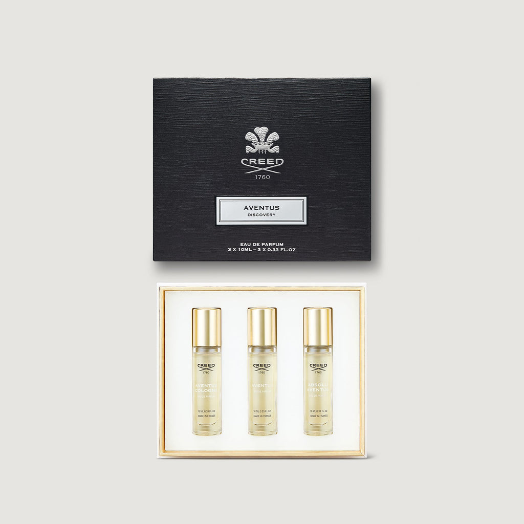 Creed Aventus perfume set with three bottles and a black box on a light gray background