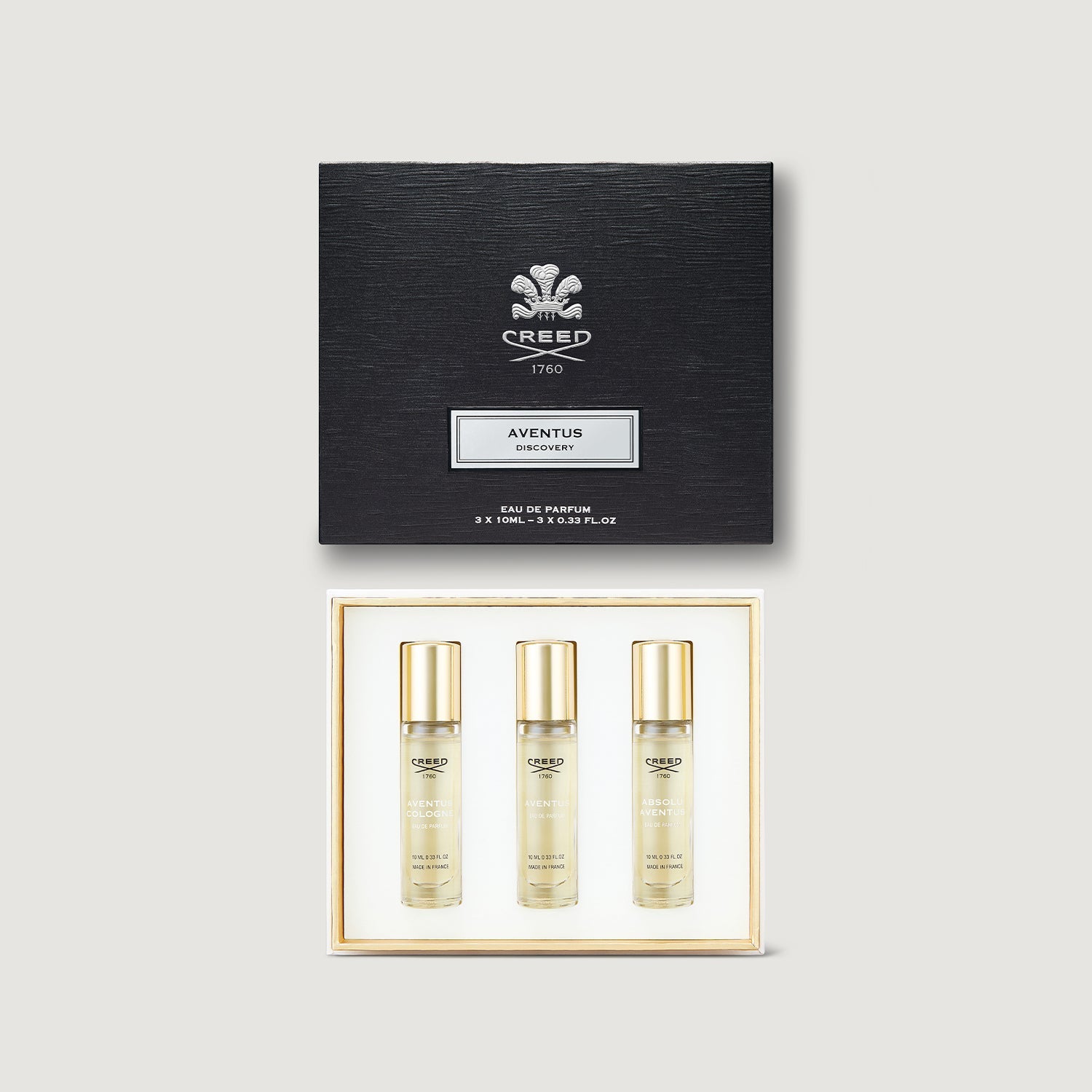 Creed Aventus perfume set with three bottles and a black box on a light gray background